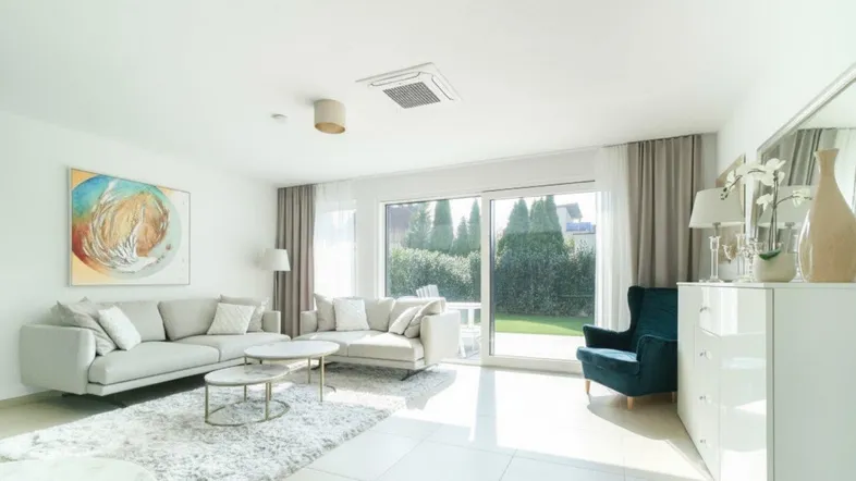 Helles Wohnzimmer mit bequemen Sofas, großem Fenster und direktem Zugang zum grünen Garten.