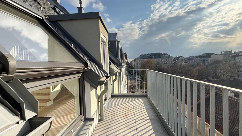 Sonniger Balkon im Dachgeschoss mit Fliesenboden und weitem Blick über die Stadt.