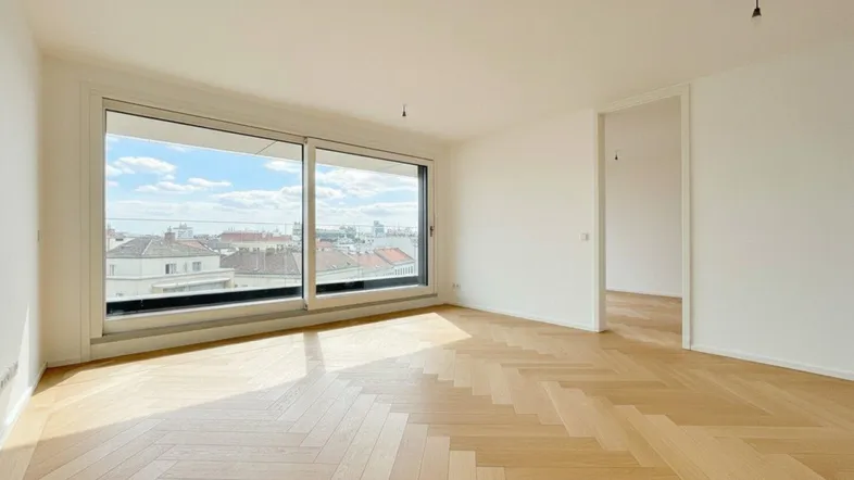Helles Zimmer mit Fischgrätparkett und großen Fenstern, die einen weiten Blick über die Stadt bieten.