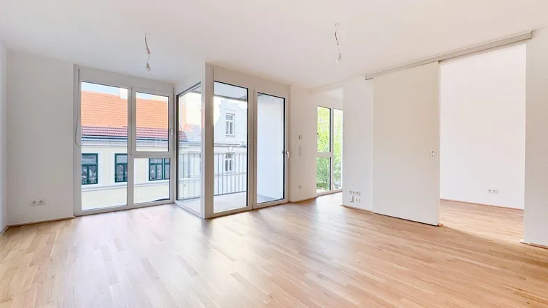 Heller, offener Wohnbereich mit großen Fenstern, Parkettboden und Zugang zu einem Balkon.
