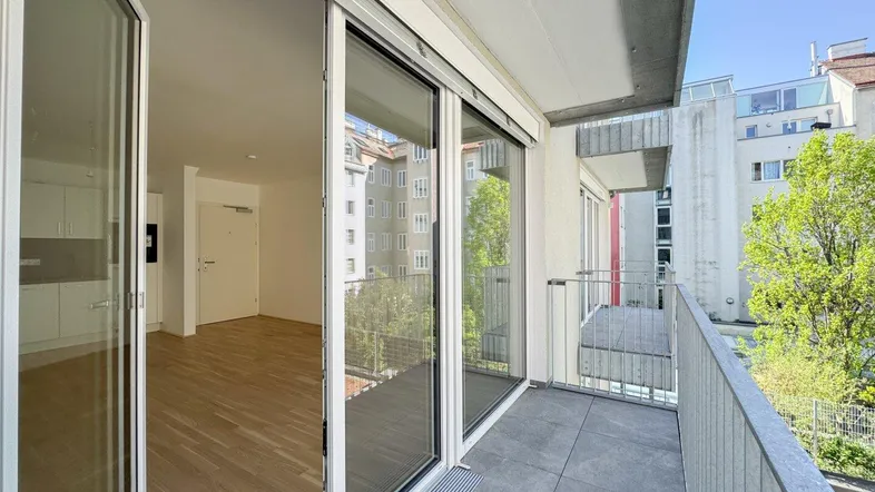 Heller Balkon mit Fliesenboden und Blick in den Wohnbereich der Wohnung.