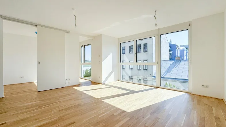 Heller Wohnbereich mit großen Fenstern, Holzboden und viel Tageslicht, bereit zur individuellen Gestaltung.