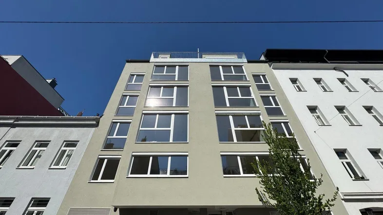 Modernes Mehrfamilienhaus mit klarer Architektur und vielen Fenstern unter blauem Himmel.