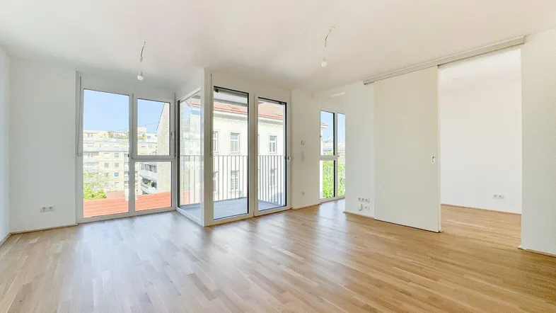Heller Wohnbereich mit Parkettboden, großen Fenstern und Zugang zu einem Balkon mit Stadtblick.