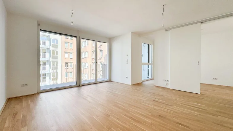 Heller Wohnbereich mit Parkettboden, großen Fenstern und Zugang zu einem Balkon mit Stadtblick.