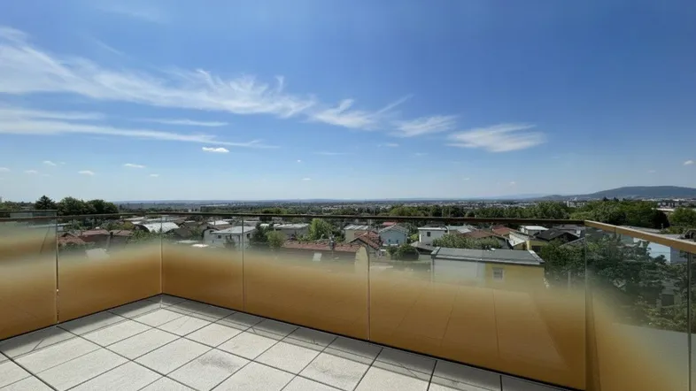 Geräumige Dachterrasse mit modernen Fliesen und Glasgeländer, die einen weiten Blick über die Stadt und die grüne Landschaft bietet.
