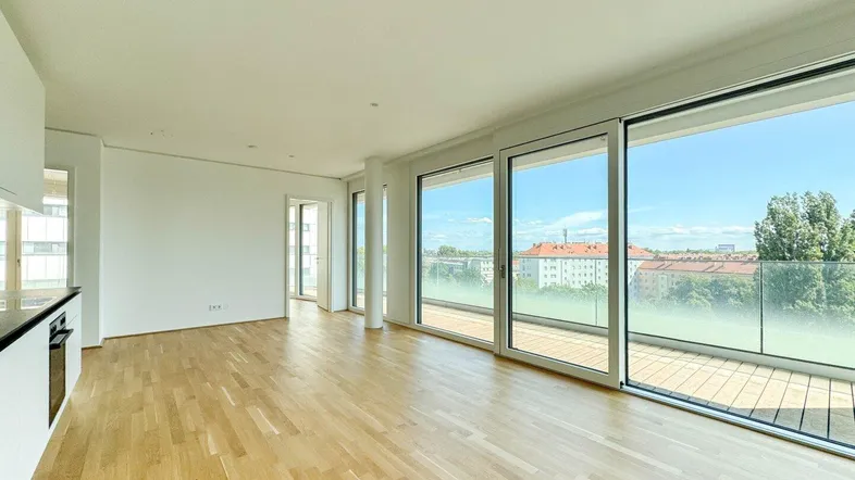 Heller, moderner Wohnbereich mit Parkettboden, großen Fenstern und Zugang zum Balkon.