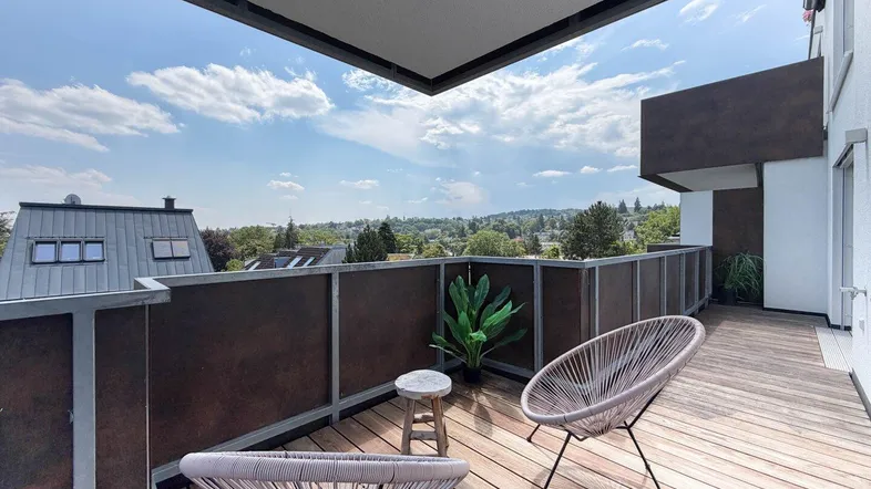 Geräumiger Balkon mit Holzboden und modernen Sitzgelegenheiten, bietet einen weiten Blick über die Umgebung.
