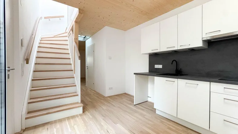 Moderne offene Küche mit weißen Schränken, Holzdecke und Treppenaufgang in hellem Ambiente.