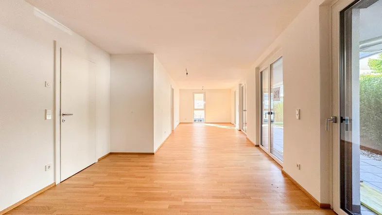 Helles, leeres Wohnzimmer mit Parkettboden und Zugang zur Terrasse.