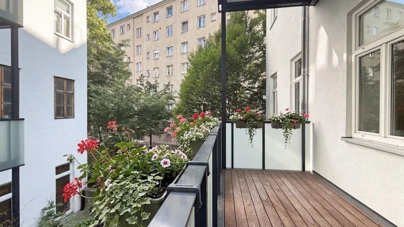 Geräumiger Balkon mit Holzboden und Blumenkästen, bietet einen Blick auf die umliegenden Gebäude und Bäume.