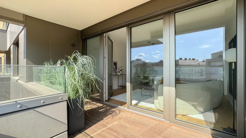 Moderner Balkon mit Holzfußboden und Glasgeländer, bietet Zugang zum hellen Innenbereich.