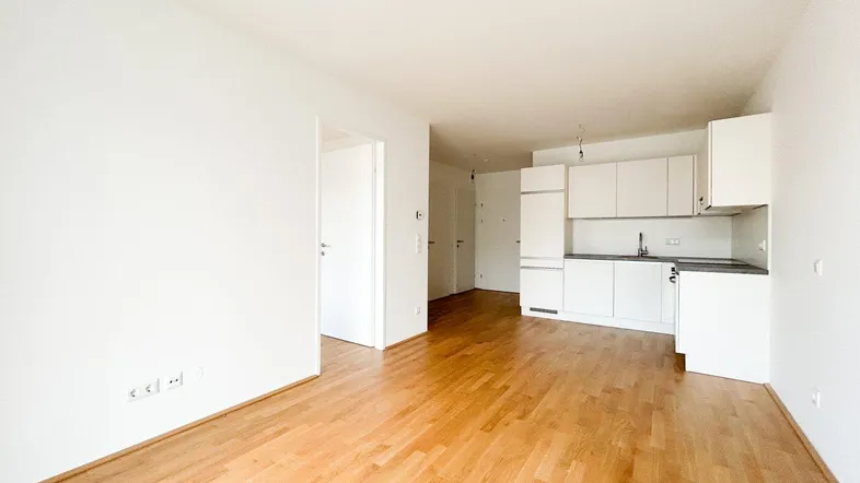 Helles, offenes Wohnzimmer mit integrierter Küchenzeile und Parkettboden.