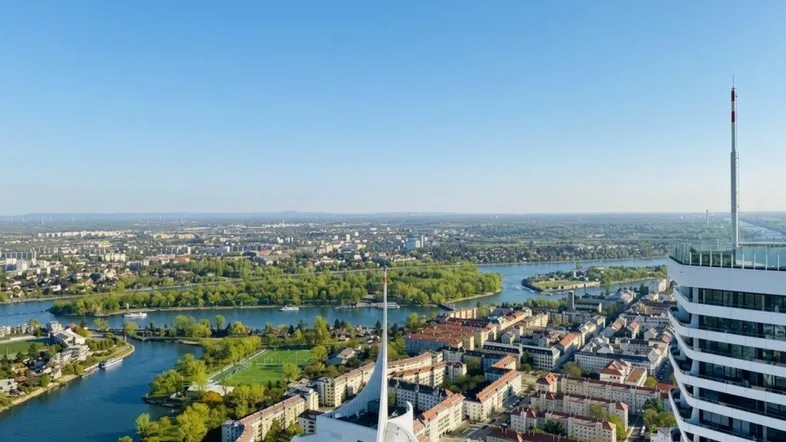 Panoramablick über die Stadt mit Fluss, grünen Ufern und modernen Hochhäusern unter blauem Himmel.