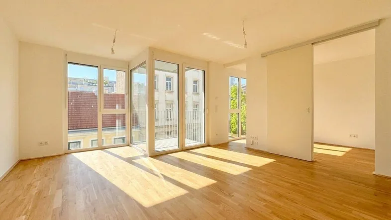 Helles Wohnzimmer mit Holzboden, großen Fenstern und Zugang zu einem Balkon.