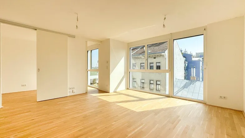 Helles und geräumiges Wohnzimmer mit Parkettboden und großen Fenstern, die viel Tageslicht hereinlassen.