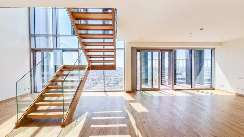 Helles, offenes Wohnzimmer mit moderner Holztreppe und raumhohen Fenstern mit Stadtblick.