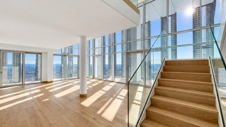 Helles, offenes Wohnzimmer mit Holzboden, raumhohen Fenstern und einer modernen Treppe.