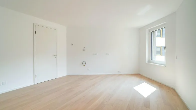Leeres Zimmer mit hellem Holzboden und weißen Wänden, ideal als Schlaf- oder Arbeitszimmer.
