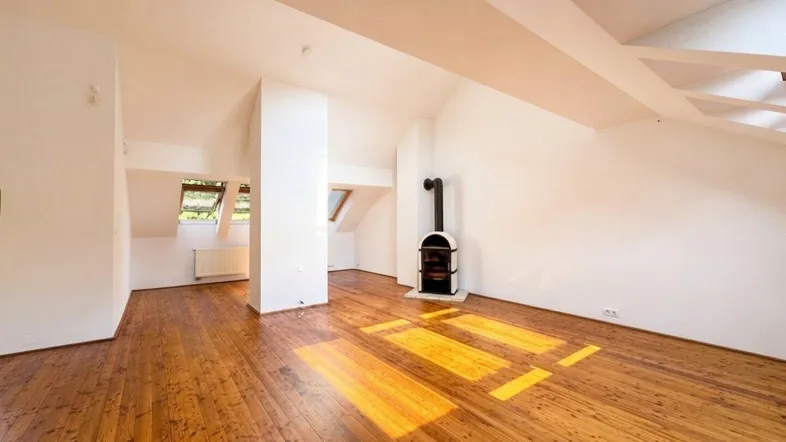 Helles Dachgeschoss-Wohnzimmer mit Holzboden, Kaminofen und schrägen Decken.