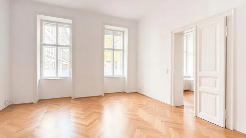 Helles, leeres Zimmer mit Fischgrätparkett und hohen Fenstern, bereit zur individuellen Gestaltung.