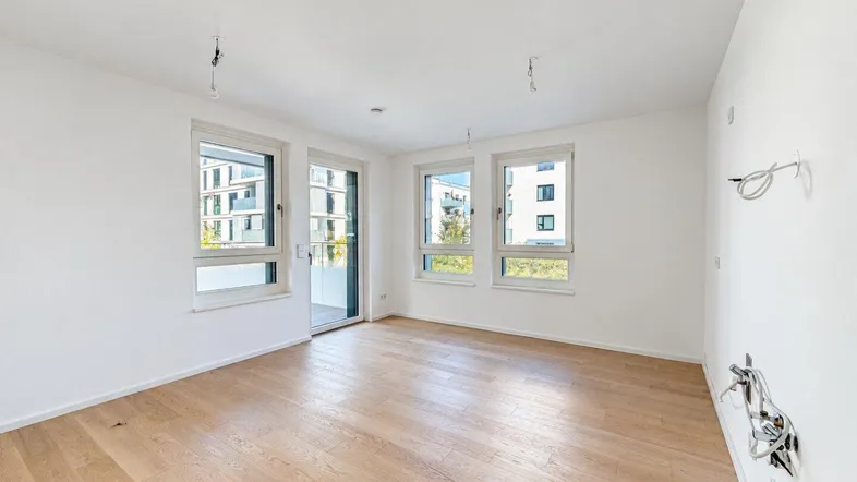 Heller, leerer Raum mit Parkettboden und Zugang zu einem Balkon oder einer Terrasse.