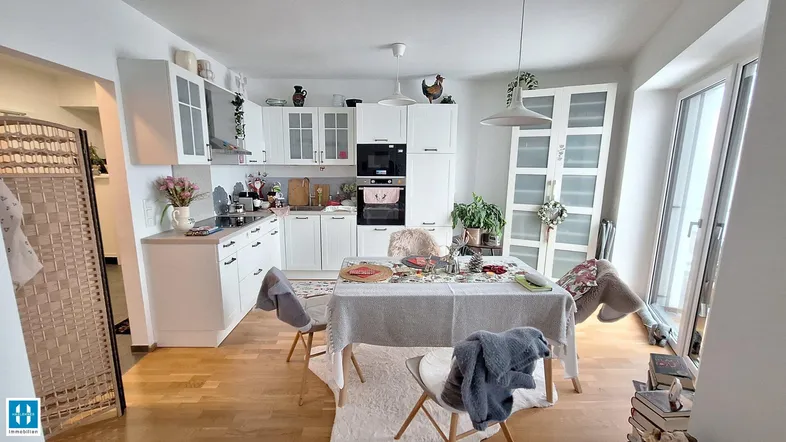 Helle, offene Küche mit weißen Schränken, Essbereich und Zugang zum Balkon.
