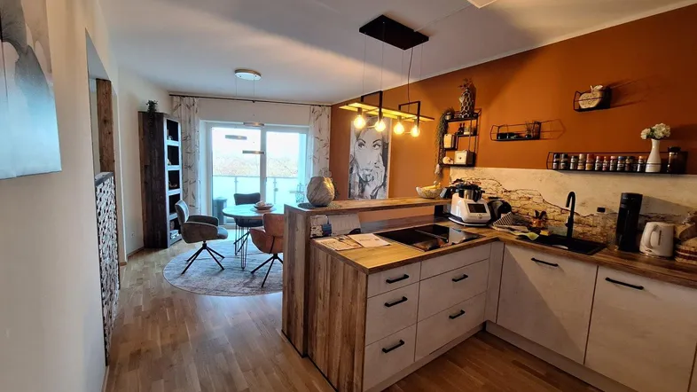 Offener Wohn-Essbereich mit moderner Küche, Holzboden und Zugang zum Balkon.