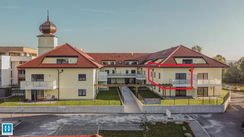 Modernes Mehrfamilienhaus mit gelber Fassade, roten Ziegeldächern und Balkonen in sonniger Umgebung.