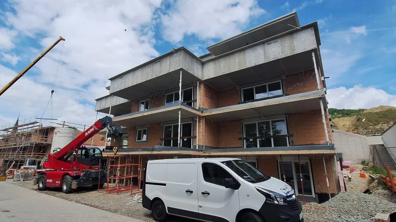 Neubau eines modernen Mehrfamilienhauses mit Balkonen im Bauzustand, umgeben von einer ländlichen Landschaft.