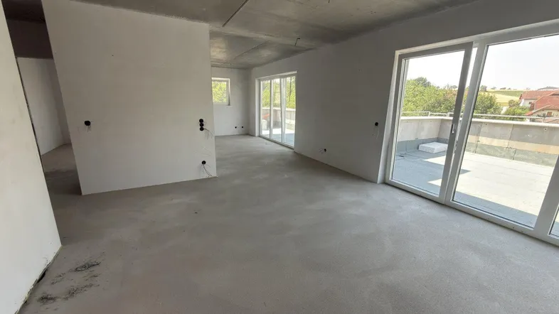 Geräumiger, unfertiger Innenraum mit Betonboden und großen Schiebetüren zur Terrasse.