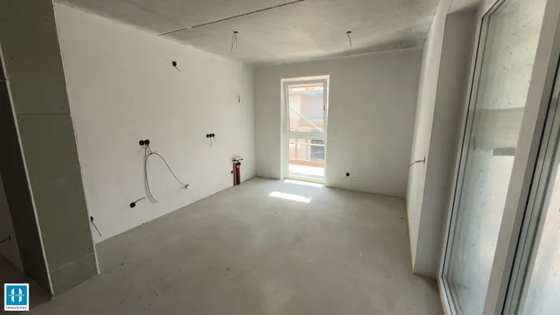 Unfertiger Innenraum mit Rohbauwänden, Betonboden und einem Fenster, das Tageslicht hereinlässt.