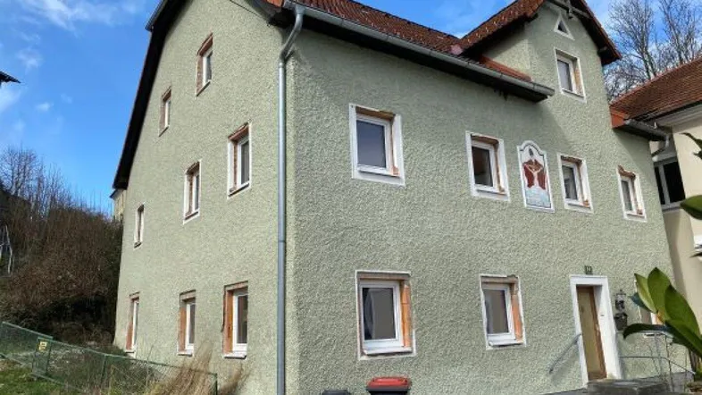 Traditionelles Wohnhaus mit hellgrüner Fassade und rotem Ziegeldach in ländlicher Umgebung.