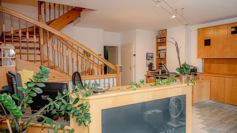 Geräumiger Bürobereich mit Holztreppe, Empfangstheke und funktionaler Einrichtung in hellem Holzton.