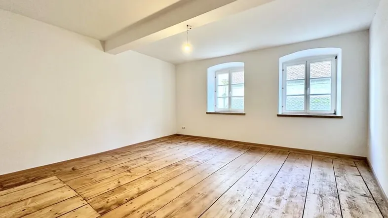 Heller Raum mit breiten Holzdielen und zwei Fenstern, ideal für individuelle Gestaltung.