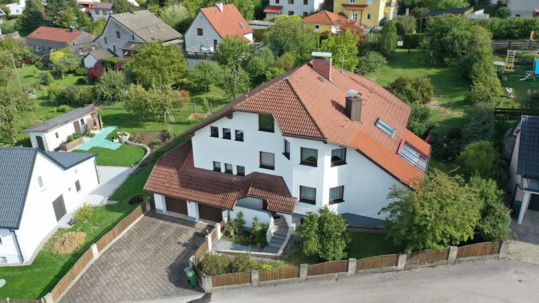 Luftaufnahme eines Einfamilienhauses mit rotem Ziegeldach und gepflegtem Garten in einer Wohnsiedlung.