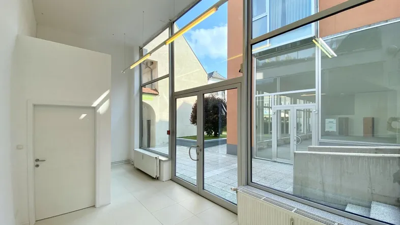 Heller Flur mit großen Glasfronten und Blick auf den Innenhof, der viel Tageslicht hereinlässt.