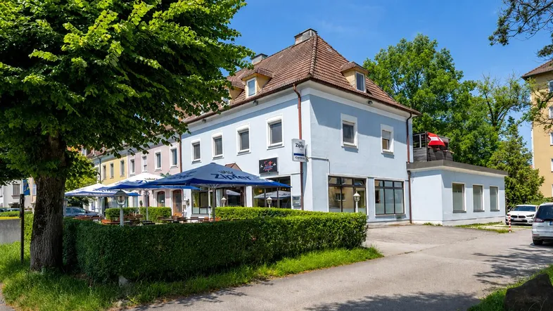 Außenansicht des Gebäudes mit einer möblierten Terrasse und Sonnenschirmen unter blauem Himmel.