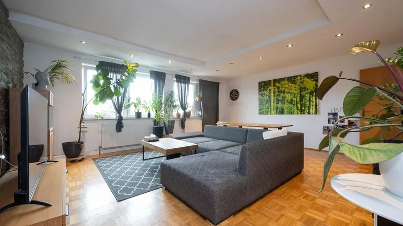 Geräumiges Wohnzimmer mit bequemer Couch, Parkettboden und dekorativer Steinwand.