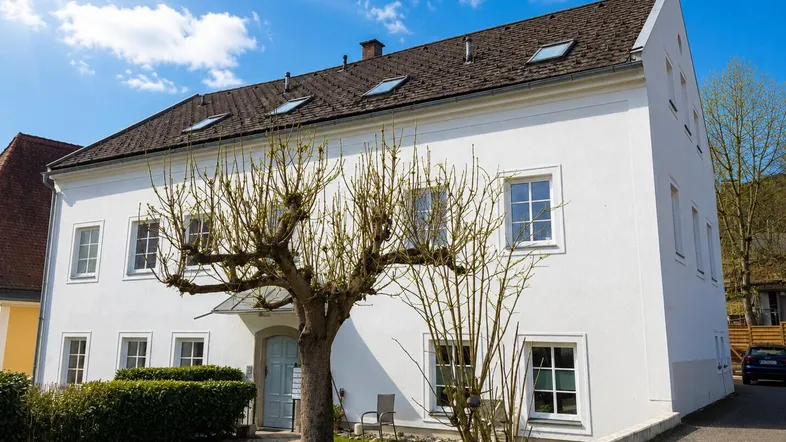 Helles, gepflegtes Altbaugebäude mit weißer Fassade, Satteldach und einem sonnigen Vorgarten.