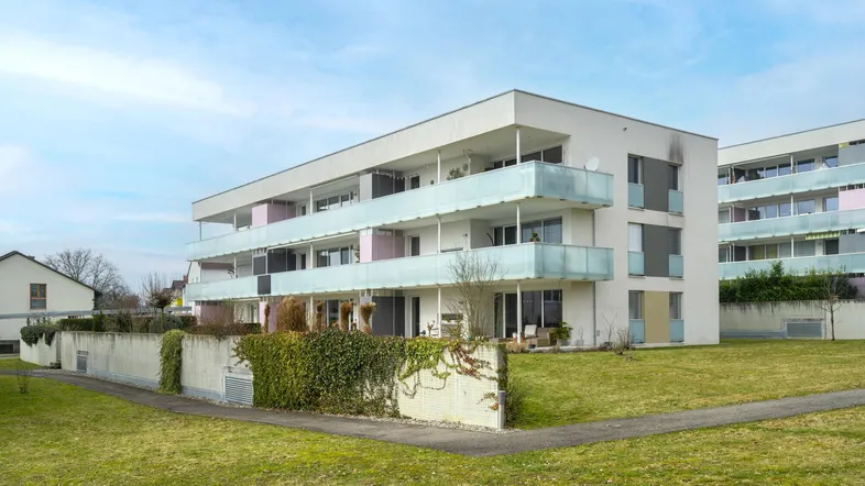 Modernes Mehrfamilienhaus mit mehreren Balkonen und gepflegter Grünfläche in einer Wohnsiedlung.