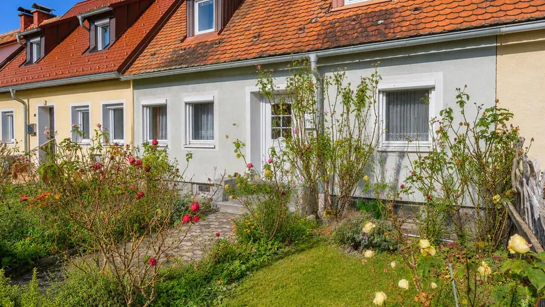 Vorderansicht eines Reihenhauses mit blühendem Vorgarten und gepflegtem Rasen.