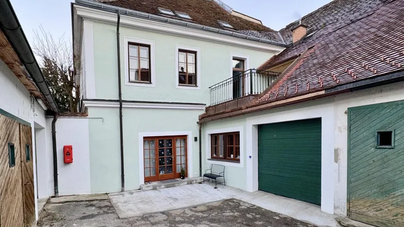 Historisches Gebäude mit hellgrüner Fassade, Holztüren und einem Garagentor in einem Innenhof.