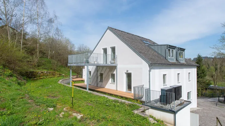 Attraktives Wohnhaus mit mehreren Terrassen und Balkonen, eingebettet in eine grüne Hügellandschaft.