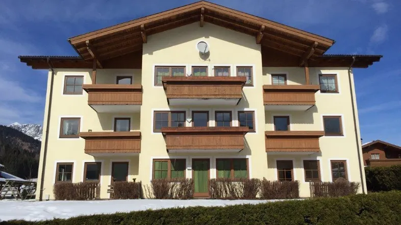 Traditionelles Mehrfamilienhaus im alpinen Stil mit mehreren Holzbalkonen und Bergblick im Winter.