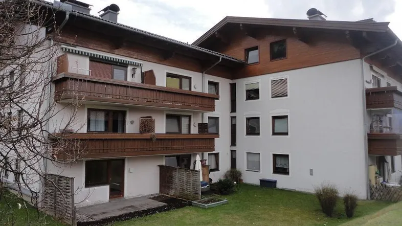 Mehrfamilienhaus mit traditioneller Architektur, Balkonen und einem kleinen Gartenbereich.