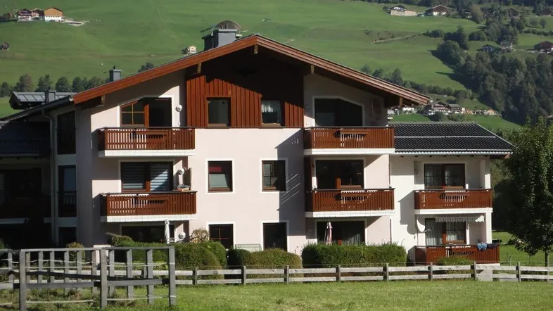 Mehrfamilienhaus im alpinen Stil mit mehreren Balkonen und Blick auf grüne Hügel.
