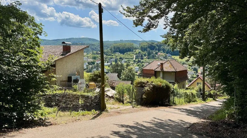 Blick auf eine ländliche Straße mit Häusern und weitreichender Aussicht auf die grüne Hügellandschaft.