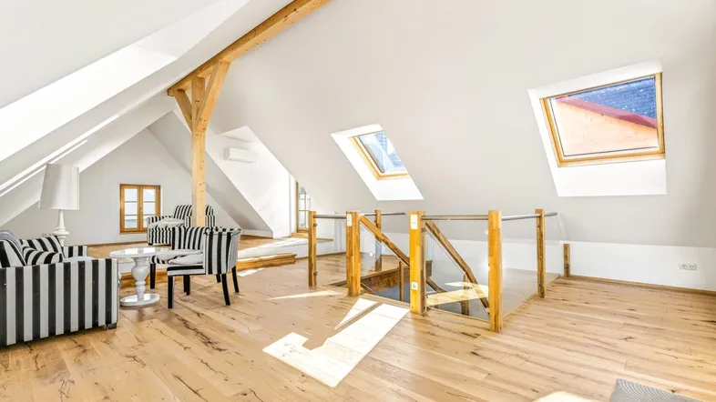 Helles Dachgeschoss-Wohnzimmer mit Holzbalken, Parkettboden und gemütlicher Sitzecke unter den Dachfenstern.