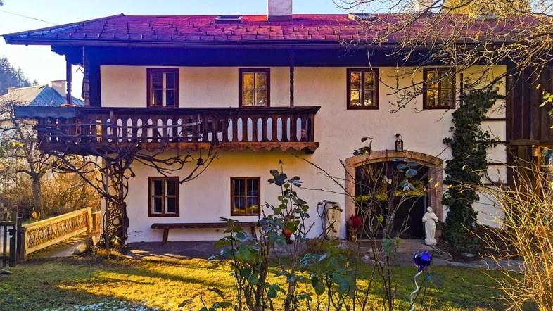Traditionelles Haus im alpenländischen Stil mit Holzbalkon und Gartenbereich im Sonnenlicht.